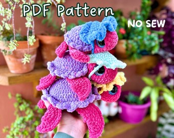 May include: A set of three crocheted turtle amigurumi patterns. The turtles are stacked on top of each other and are made in shades of pink, purple, blue, and yellow. The pattern is a PDF download and is a no-sew project.