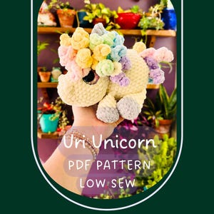 May include: A handmade, plush unicorn toy in soft yellow, with a rainbow mane and tail. The unicorn is being held in a person's hand. Text on the image reads "Uri Unicorn PDF Pattern LOW SEW".
