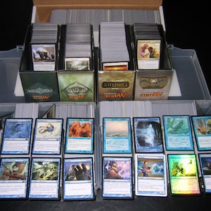 May include: A collection of Magic: The Gathering cards organized in clear plastic boxes. The boxes are labeled with the set names "Conflux", "Shards of Alara", and "Zendikar". The cards are arranged in rows and columns, with the card backs facing up.