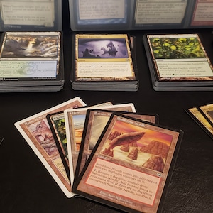 May include: A collection of Magic: The Gathering cards, including a variety of lands, spells, and creatures. The cards are arranged in stacks and fanned out on a black surface.