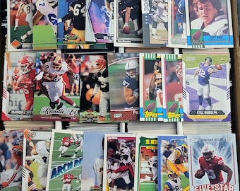 May include: A collection of sports trading cards featuring various football players. The cards are in various colors, including red, blue, green, and white. The cards feature images of the players, their names, and team logos. The cards are arranged in rows and columns on a table.