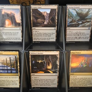 May include: A display of Magic: The Gathering trading cards, featuring various land cards. The cards are in individual black display slots. The cards have colorful fantasy art and text descriptions.