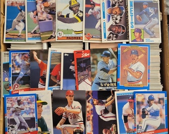 May include: A collection of baseball trading cards featuring various players from different teams. The cards are arranged in rows and columns, with some cards showing players in action and others showing portraits. The cards are in various colors, including blue, red, white, and green.