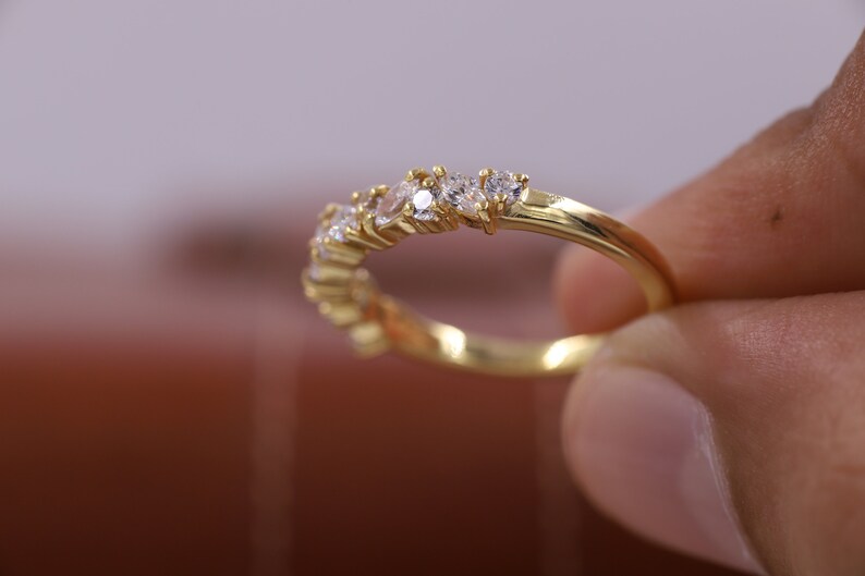 Pu&ograve; includere: Un anello a fascia d'oro con una fila di piccole pietre preziose trasparenti.