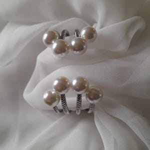 May include: A silver bracelet with five white pearl accents. The bracelet is made of a twisted metal design.