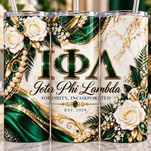 May include: A cylindrical tumbler featuring a white marble background with green and gold accents. The design includes white roses, pearl strands, and green gemstones. The text reads Iota Phi Lambda Sorority, Incorporated, Est. 1929 in gold lettering.