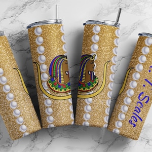 May include: Four gold glitter tumblers with a white pearl design. Each tumbler features a colorful illustration of an Egyptian queen with a gold crown and a blue and green headdress. One tumbler has the text "Dr. T. Scales" in blue.