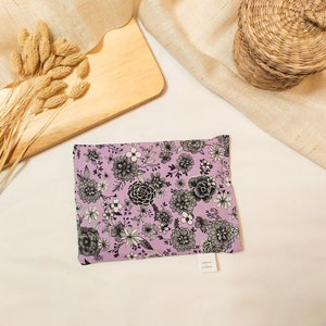 Peut inclure: Une petite pochette en tissu lavande avec un imprimé floral noir et blanc. La pochette a une petite étiquette blanche avec le texte "Made by Whisper"