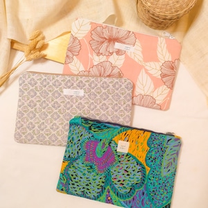 Può includere: Tre pochette con cerniera con diversi motivi floreali. Le pochette sono in tessuto e hanno una chiusura a zip. Le pochette sono su una superficie bianca.