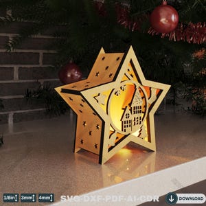 May include: A wooden star-shaped Christmas decoration with a cutout design of a house inside a circle. The star has small star cutouts and is illuminated from within. The image also includes text that reads "1/8in 3mm 4mm SVG-DXF-PDF-AI-CDR" and a download button.