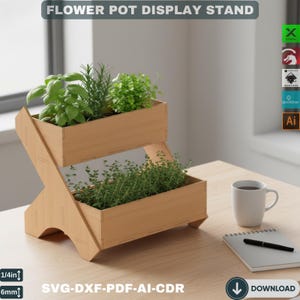 May include: A two-tiered wooden flower pot display stand with the text "FLOWER POT DISPLAY STAND". The stand holds various green herbs. A white mug, notepad, and pen are on the table. The stand is 1/4 inch (6mm) thick and is available in SVG-DXF-PDF-AI-CDR formats.
