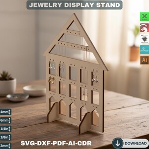 May include: A wooden house-shaped jewelry display stand with holes and slots for earrings and necklaces. The text "JEWELRY DISPLAY STAND" is at the top. The stand is on a wooden surface. Measurements are in mm and inches.