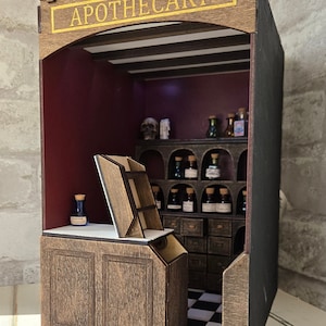 May include: A miniature wooden apothecary shop with a sign that reads "APOTHECARY" in gold lettering. The shop has a dark wood counter, shelves filled with small glass bottles, and a checkered floor.