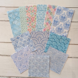 May include: A collection of twelve square fabric napkins featuring various patterns including blue and white scalloped designs, geometric shapes, floral motifs, and wavy lines in shades of blue, green, pink, and white, arranged in a fan-like display.