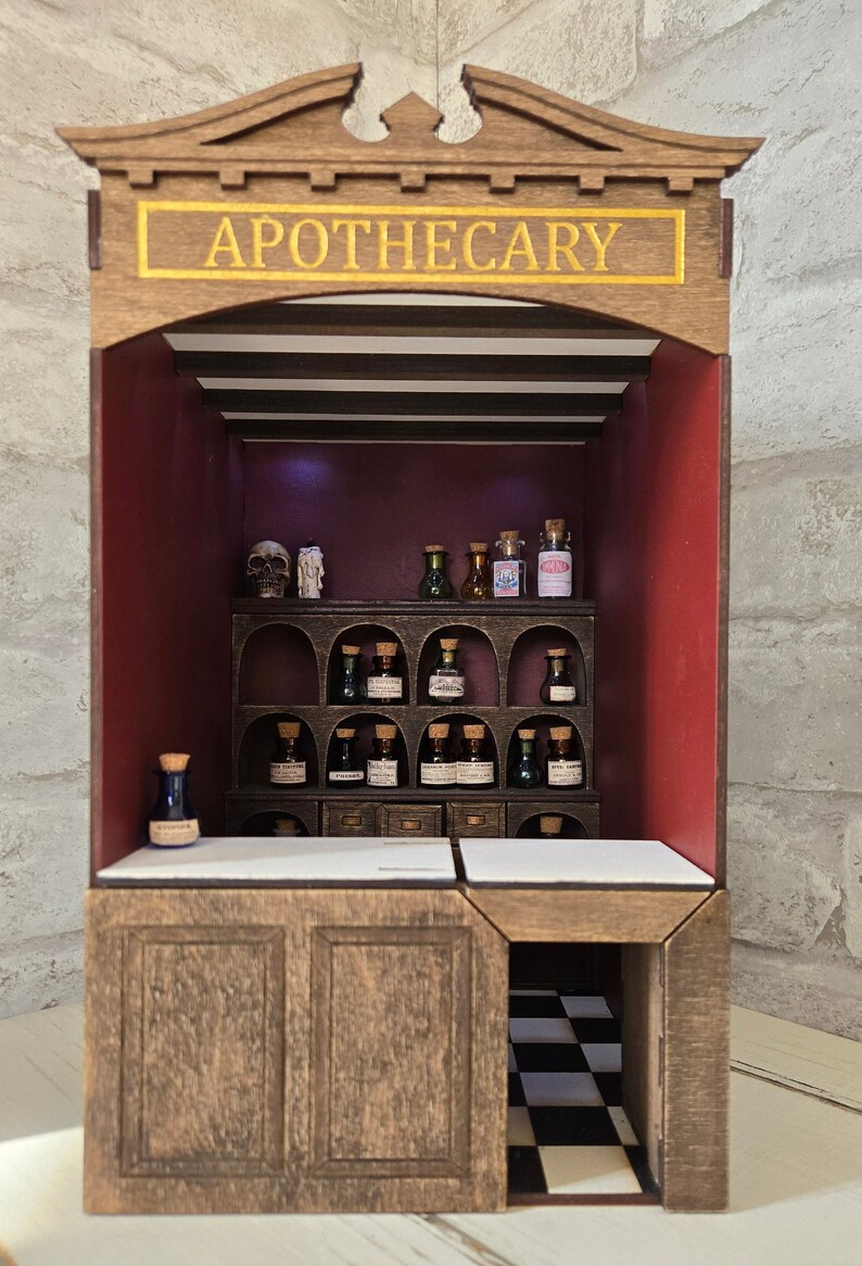 May include: A miniature wooden apothecary shop with a sign that reads "APOTHECARY" in gold lettering. The shop has a counter, shelves, and a small back room with a checkered floor. There are many small glass bottles filled with colorful liquids on the shelves.