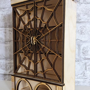 Puede incluir: Un gabinete de madera con un dise&ntilde;o de telara&ntilde;a decorativo y una luna creciente y un pentagrama en la parte superior. El gabinete tiene dos puertas y un estante debajo.