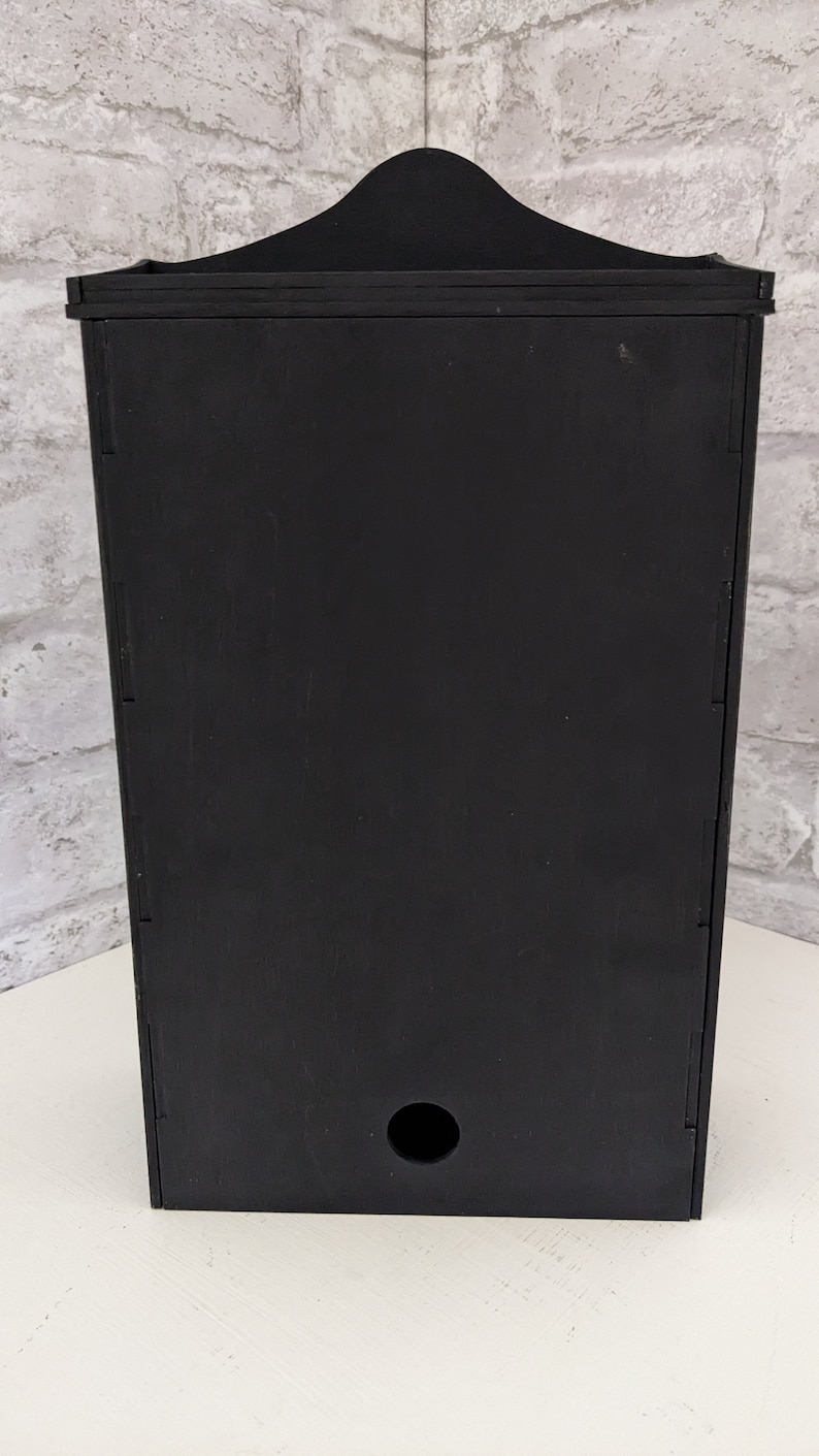 Puede incluir: Caja de pared de madera negra con un peque&ntilde;o agujero en la parte inferior.