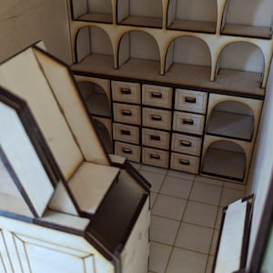 May include: A miniature wooden model of a room with a shelf unit featuring arched openings and drawers. The room has a tiled floor and a wooden door.