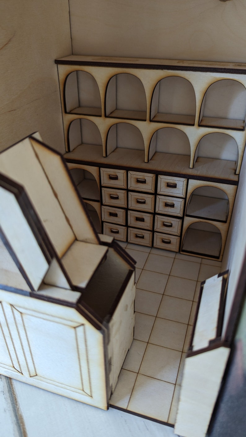 May include: A miniature wooden model of a room with a shelf unit featuring arched openings and drawers. The room has a tiled floor and a wooden door.