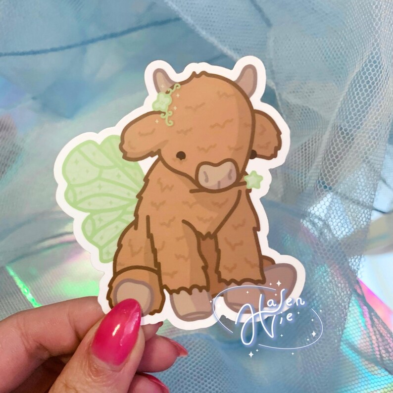 May include: A brown and white fuzzy cow with green fairy wings. The cow is sitting on its hind legs and has a flower crown on its head.