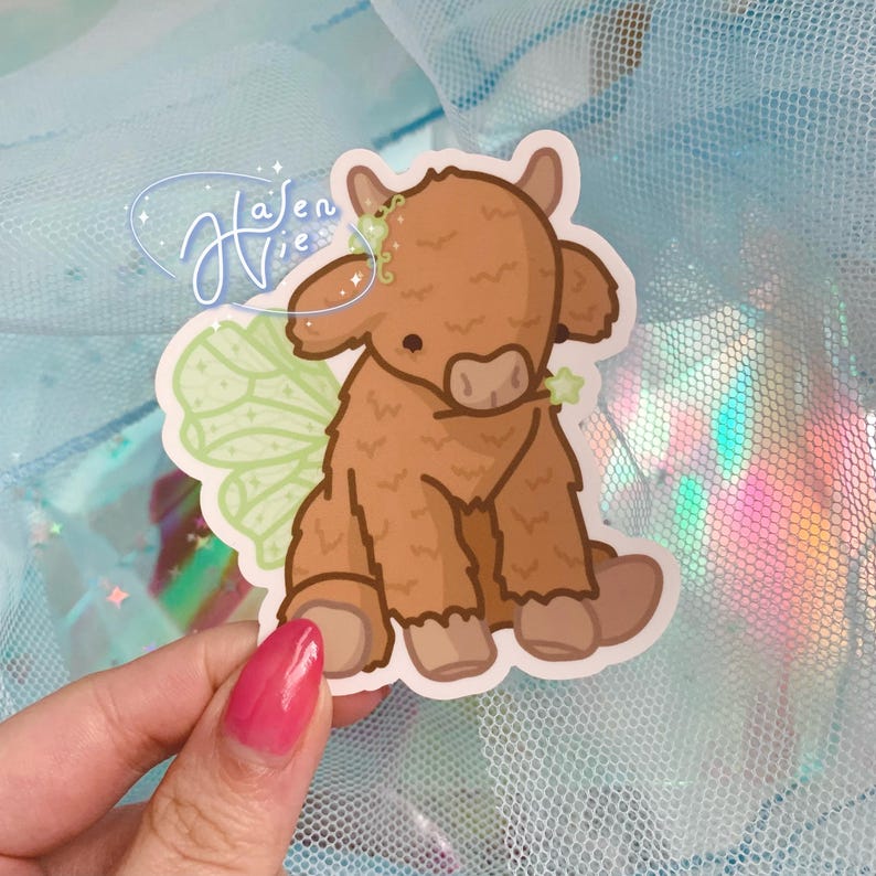 May include: A brown and white Highland cow with green fairy wings. The cow is sitting down and has a cute expression on its face.