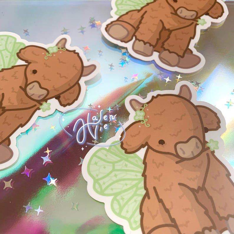 May include: Three brown and white cartoon highland cow stickers with green fairy wings. The stickers have a whimsical and cute style.