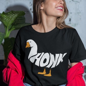 May include: A black t-shirt featuring a white graphic of a goose with the word "HONK" spelled out in the goose's body.