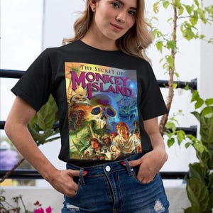 May include: A black t-shirt with a colorful graphic of the video game "The Secret of Monkey Island". The graphic features a skull, a pirate ship, and several characters.