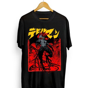 May include: Black t-shirt featuring a red and gray illustration of a demon with wings and horns. The graphic is set against a red background with Japanese text in yellow. The shirt is hanging on a wooden hanger.