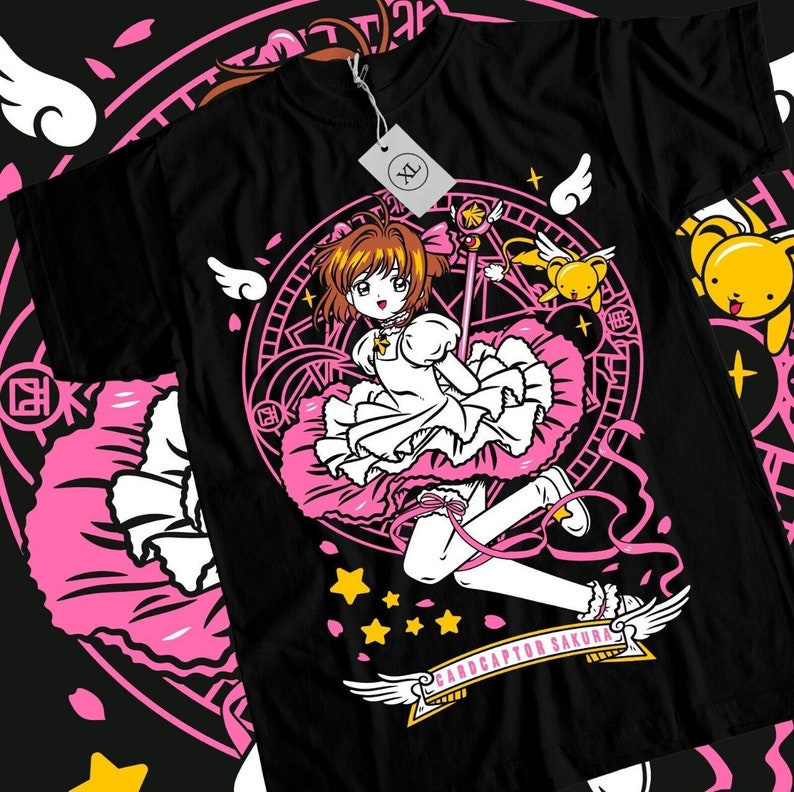 May include: Black t-shirt with a pink and white graphic of a girl with a wand and a pink dress. The graphic also includes a circle with stars and the text "Cardcaptor Sakura".