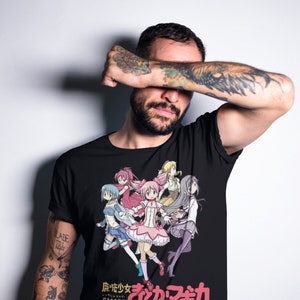 May include: Black t-shirt with a colorful anime graphic of five girls in pink, blue, yellow, and purple outfits. The text "Puella Magi Madoka Magica" and "まどか☆マギカ" are printed on the shirt.