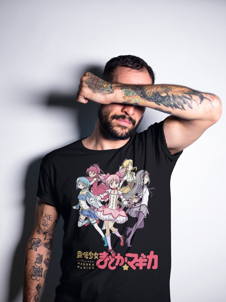 May include: Black t-shirt with a colorful anime graphic of five girls in pink, blue, yellow, and purple outfits. The text "Puella Magi Madoka Magica" and "まどか☆マギカ" are printed on the shirt.