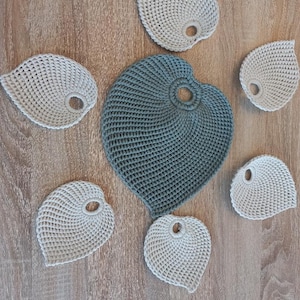 Può includere: Sette sottobicchieri a forma di foglia all'uncinetto in due colori: beige chiaro e blu scuro. I sottobicchieri sono disposti in cerchio su una superficie di legno.