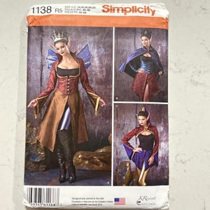 May include: Simplicity costume pattern featuring three fantasy-themed outfits. The costumes include long-sleeved tops, skirts, and capes, with details like pointed ears and crowns. The pattern includes sizes 14, 16, 18, 20, and 22.
