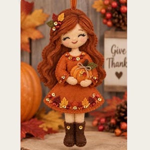May include: A felt hanging ornament of a girl with long wavy auburn hair, wearing an orange dress decorated with sequins and autumn leaves. The figure holds a small orange pumpkin and wears brown boots. The dress hem features leaf accents.