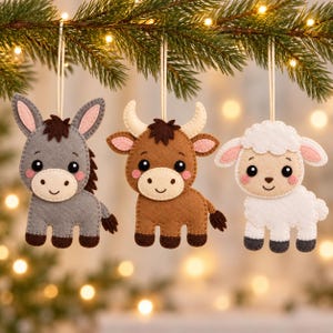May include: Three felt hanging ornaments shaped like a donkey, a bull, and a sheep. The donkey is gray, the bull is brown with cream horns, and the sheep is white with a textured wool appearance. Each animal has black eyes, pink cheeks, and a string.