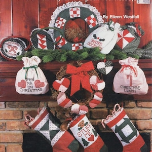 May include: A book cover titled "A Patchwork Christmas" featuring various Christmas-themed patchwork projects. The image showcases a wreath, stockings, and gift bags with festive designs and text like "Santa's Goods" and "Christmas Loot".
