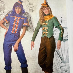 May include: Two people wearing Wizard of Oz-themed costumes. One costume is a blue outfit with a zig-zag design and matching hat. The other is a green jacket with bow accents, brown pants, and a small hat. The background features hot air balloon illustrations.
