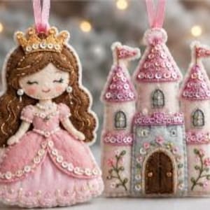 Op de afbeelding: Twee viltornamenten bestaande uit een prinses met bruin haar, een gouden kroon en een roze jurk, en een roze kasteel met drie torens, pailletten en geborduurde bloemaccenten. Beide ornamenten zijn voorzien van roze linten om op te hangen.