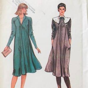 May include: Two vintage dress patterns are shown. The first dress is teal with long sleeves and a collared neckline. The second dress is gray with a white collar and a black bow. Both dresses have a knee-length hemline.