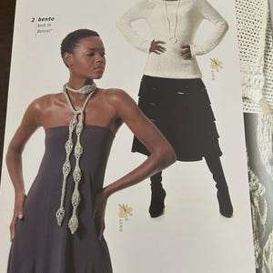 May include: A woman models two knit designs. One is a long, flowing, dark purple dress with a decorative, open-weave, light-colored scarf. The other is a cream-colored sweater with a black tiered skirt and a long necklace.