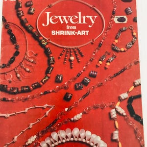 May include: A red background showcases various handmade jewelry pieces. The image features necklaces, bracelets, and earrings with beads in various colors and shapes. The text "Jewelry from SHRINK-ART" is prominently displayed in white.
