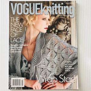 May include: A Vogue Knitting International magazine cover featuring a woman wearing a gray lace wrap. The cover text includes "The New Face of Lace" and "Wrap Star!" with additional text about romantic cardigans and beach chic.