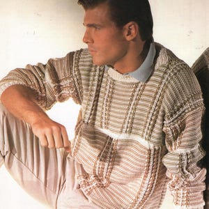May include: A knitted sweater in shades of beige, brown, and white. The sweater features a crew neck and a striped pattern with vertical and horizontal elements. The sleeves have a textured design. The person is wearing light-colored pants.