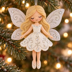 May include: A felt fairy ornament with blonde hair, wearing a white dress adorned with silver embroidery and clear rhinestones. The fairy has large white felt wings decorated with silver stitching and rhinestones, and wears matching white ballet slippers.
