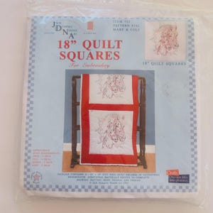 May include: A package of 18-inch quilt squares for embroidery, featuring a design of two horses. The package includes the text "18" QUILT SQUARES" and "MARE & COLT". The quilt squares are displayed on a wooden rack.