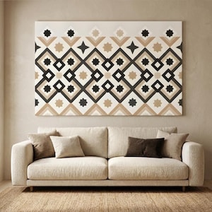 Puede incluir: Un sofá beige con varias almohadas sobre una alfombra tejida. Encima del sofá hay un gran lienzo rectangular con un patrón geométrico en colores negro, beige y crema.