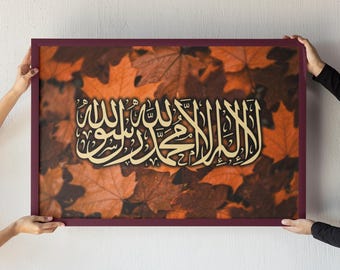 Könnte beinhalten: Ein gerahmtes Kunstwerk mit goldener arabischer Kalligraphie vor einem Hintergrund aus orangefarbenen und braunen Herbstblättern. Der Rahmen hat eine tief burgunderrote Farbe. Das Kunstwerk wird von zwei Händen gehalten.