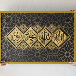 May include: A framed Islamic art piece with Arabic calligraphy in gold and black. The artwork features geometric patterns and is held by two sets of hands. The frame is a gold color.