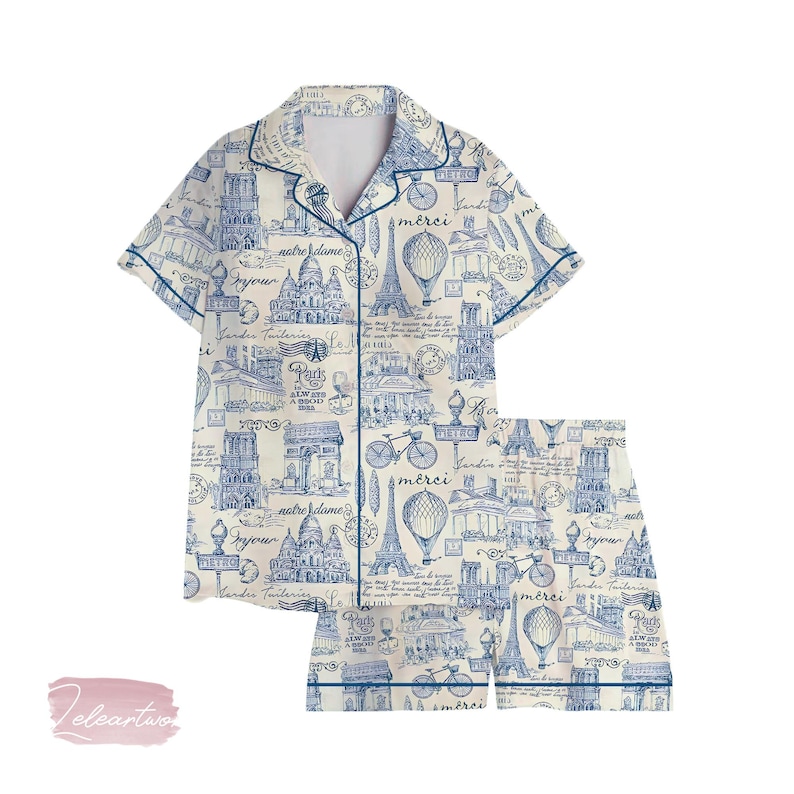 K&ouml;nnte beinhalten: Ein zweiteiliges Pyjama-Set mit cremefarbenem Hintergrund und blauem Pariser-Themen-Druck. Der Druck zeigt den Eiffelturm, Hei&szlig;luftballons, Fahrr&auml;der und architektonische Wahrzeichen. Das Set hat ein Hemd mit Kn&ouml;pfen und Shorts.